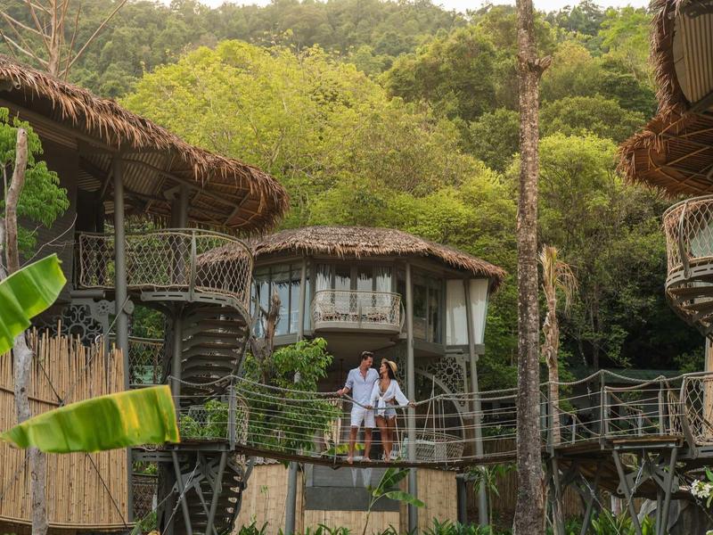 Due persone su un ponte tra case di legno in un resort nella foresta verde.