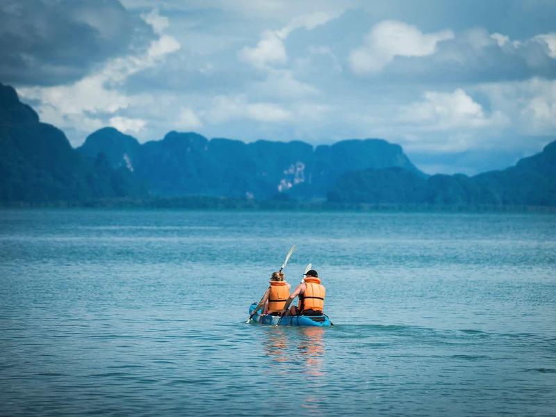 Due persone con giubbotti di salvataggio pescano su una barca con montagne sullo sfondo.