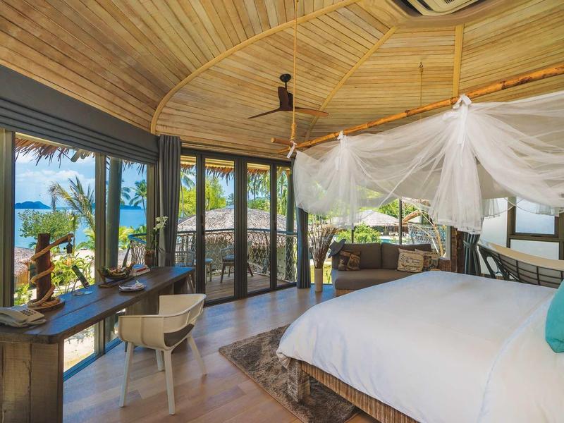 Camera da letto con soffitto in legno e letto con zanzariera, grandi finestre con vista mare.