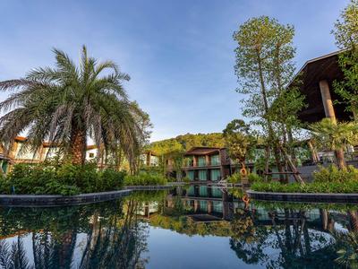 Jardin d'hôtel avec piscine et végétation tropicale luxuriante sous un ciel clair.
