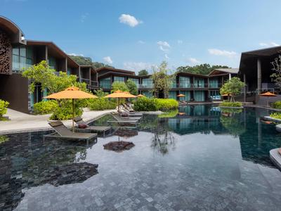 Piscine d'hôtel moderne avec transats et parasols au milieu d'un jardin verdoyant sous un ciel clair.