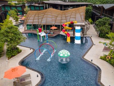 Moderní venkovní bazén s tobogány, vodními fontánami a hřištěm, obklopený posezením hotelu.