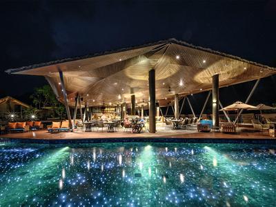 Moderní hotelová restaurace s osvětleným bazénem v noci a jedinečným designem střechy.