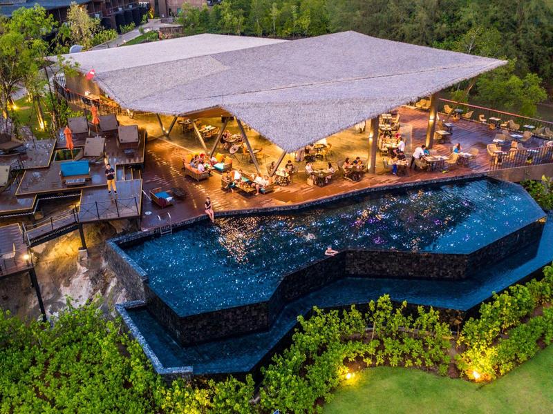 Luxusní venkovní prostor s víceúrovňovým bazénem a zastíněným salonkem v hotelové zahradě v noci.