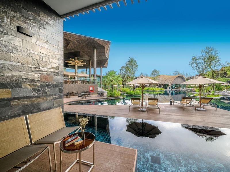 Luxusní terasa u bazénu s lehátky, slunečníky a moderní kamennou fasádou pod modrou oblohou.