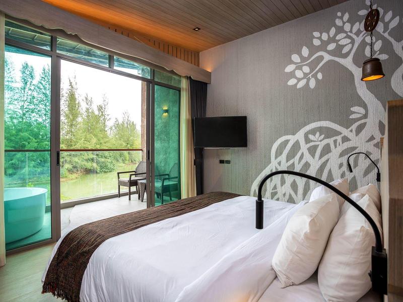 Moderní hotelový pokoj s velkým oknem, dvoulůžkem a výhledem na zelený venkovní prostor.