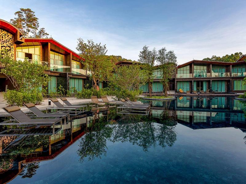 Moderní rekreační areál s bazénem, lehátky a zeleným okolím za jasné oblohy.