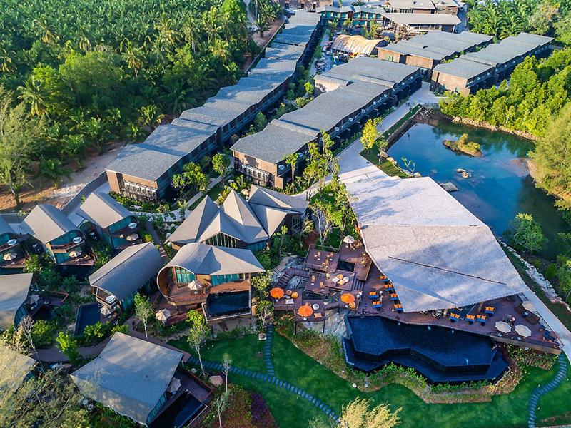 Letecký pohled na resort s moderními budovami, bazénem a množstvím zeleně kolem.