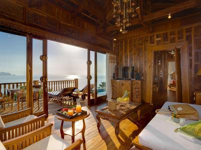 Camera d'hotel luminosa con mobili in legno, balcone e vista sulle montagne al tramonto.