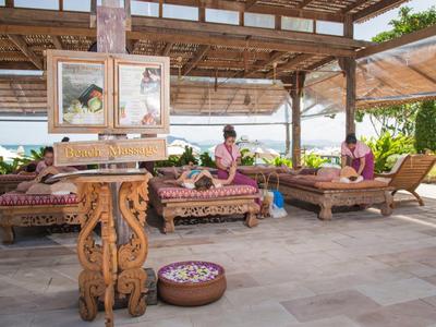 Sala massaggi all'aperto con lettini intagliati e ciotole di fiori in un ambiente tropicale.