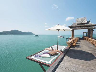 Drewniany pomost z miejscami do siedzenia, parasolem i widokiem na turkusowe morze i wyspy.