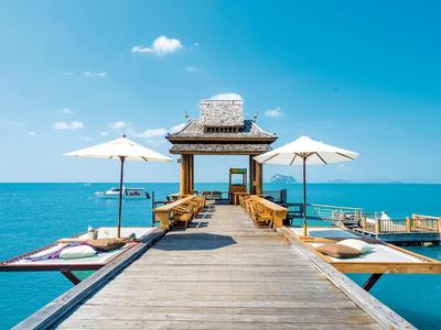 Un molo di legno con sedie e ombrelloni che conduce a un padiglione sul mare.