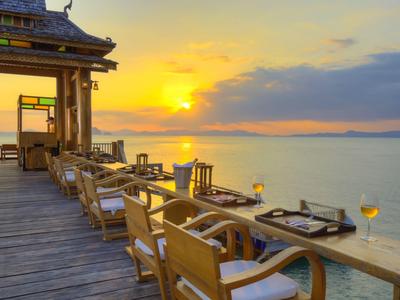 Drewniany taras z stołami i krzesłami z widokiem na morze i zachód słońca.