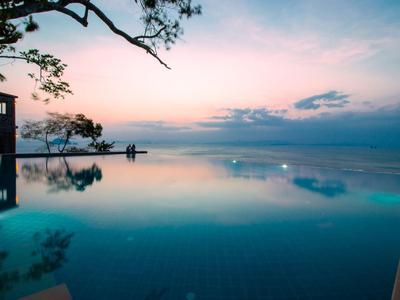 Piscina a sfioro con vista sull'oceano calmo al tramonto in un resort.