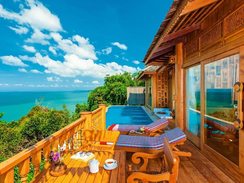 Piscina a sfioro con vista sul mare e colline boschive sotto un cielo sereno.