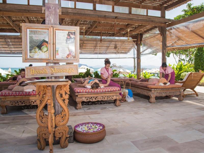 Sala massaggi all'aperto con lettini intagliati e ciotole di fiori in un ambiente tropicale.