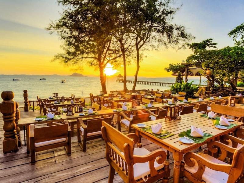Terrazza in legno con tavoli e sedie a mare al tramonto