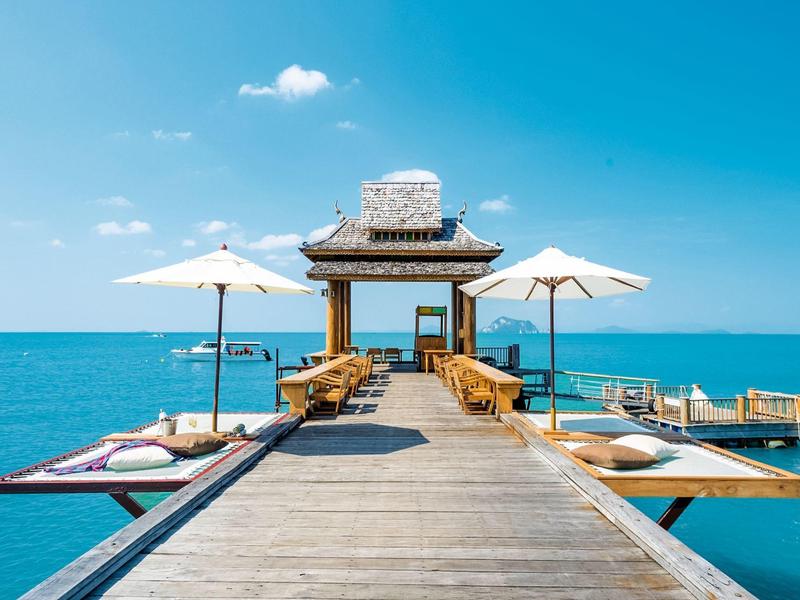 Un molo di legno con sedie e ombrelloni che conduce a un padiglione sul mare.