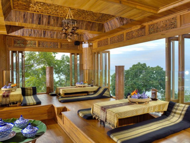 Area lounge accogliente con mobili in legno e grandi finestre con vista sul mare in un hotel tropicale.