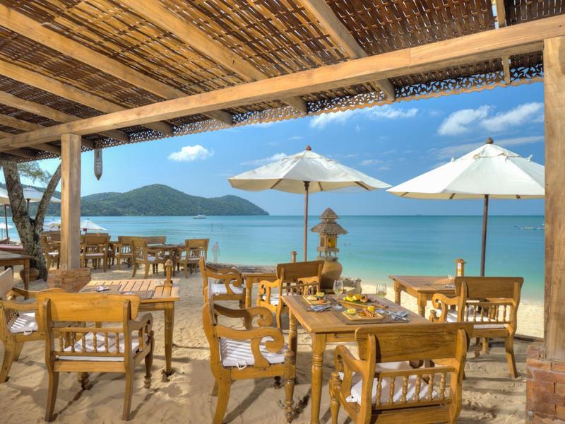 Ristorante all'aperto con mobili in legno, ombrelloni e vista sul mare e sulle montagne.