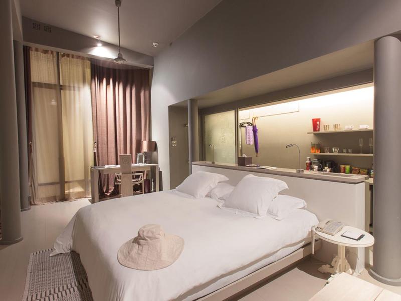 Modernes Hotelzimmer mit großem Bett, Schreibtisch und Küchenzeile in neutralen Farben.