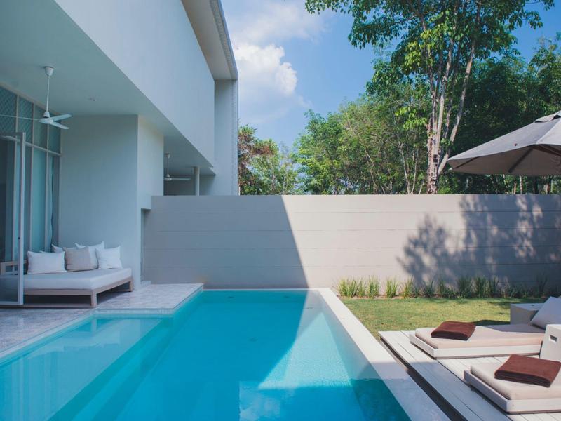 Moderner Poolbereich mit Sonnenliegen und schattigem Schirm neben einem weißen Gebäude.