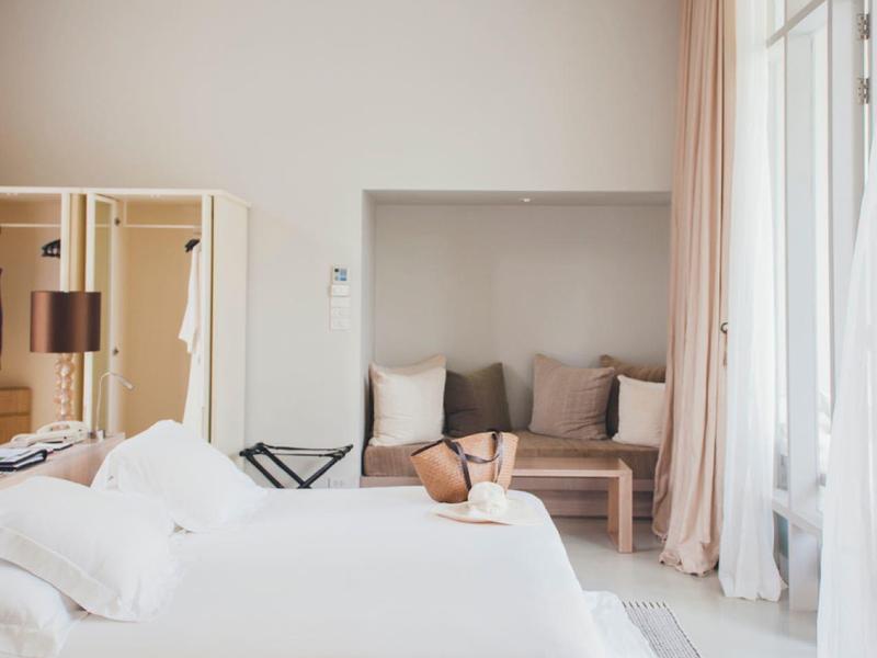 Hell eingerichtetes Hotelzimmer mit großem Bett, Sofa und Vorhängen am Fenster