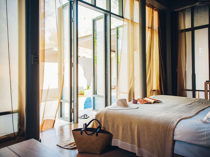 Helles Schlafzimmer mit offenem Glasfenster und Blick auf Terrasse und Pool.