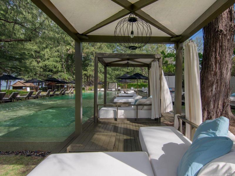 Moderne weiße Loungemöbel unter schattigen Pavillons im Garten eines Hotels.