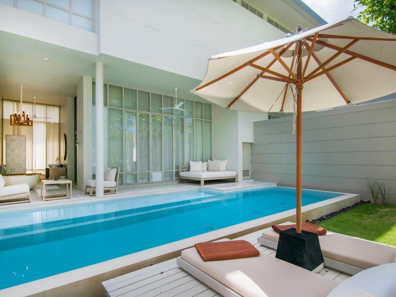 Moderner Außenbereich mit privatem Pool, Sonnenschirm und Liegestühlen neben einem Hotelzimmer.