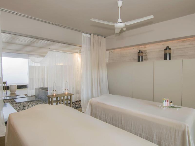 Helles Behandlungszimmer mit zwei Massageliegen und Sicht auf einen Whirlpoolbereich.