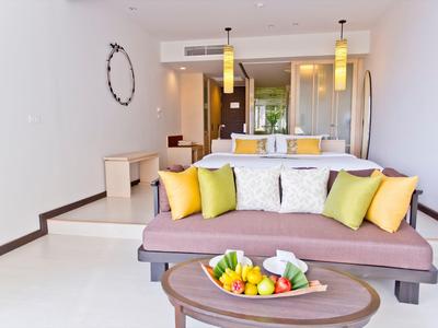 Chambre d'hôtel aménagée moderne avec canapé, coussins et assiette de fruits sur la table.