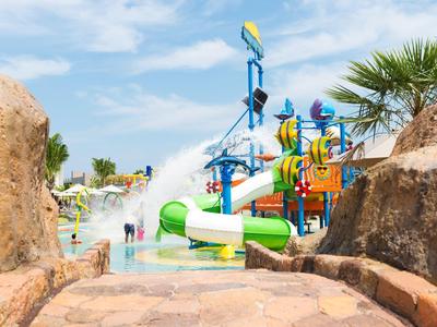 Parc aquatique avec toboggans, structures de jeu colorées et palmiers sous un ciel bleu.