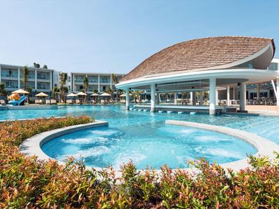 Piscine moderne avec bar swim-up et végétation environnante dans un complexe sous un ciel ensoleillé.