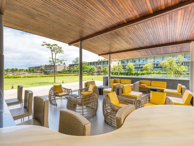 Lounge coperta con sedie in rattan e cuscini gialli accanto a una piscina e prati verdi.