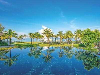 Une piscine tropicale avec des palmiers et un ciel bleu dans un complexe hôtelier.