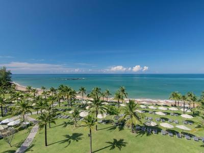 Vue d'une plage tropicale avec des palmiers, des transats et une mer bleue sous un ciel dégagé.