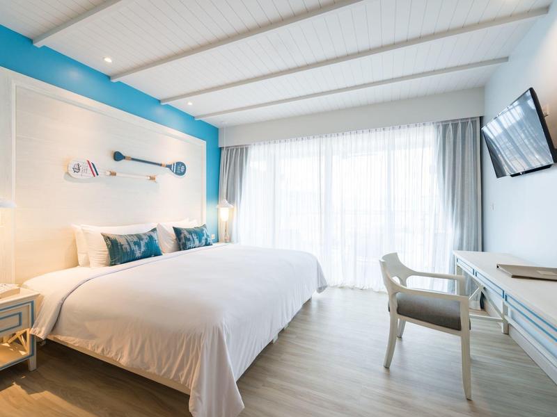 Chambre d'hôtel lumineuse avec grand lit, accents bleus et télévision à écran plat murale.