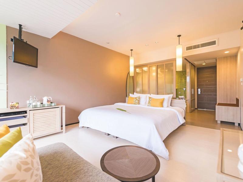 Chambre d'hôtel lumineuse avec grand lit, coin salon et décoration moderne aux tons chauds.