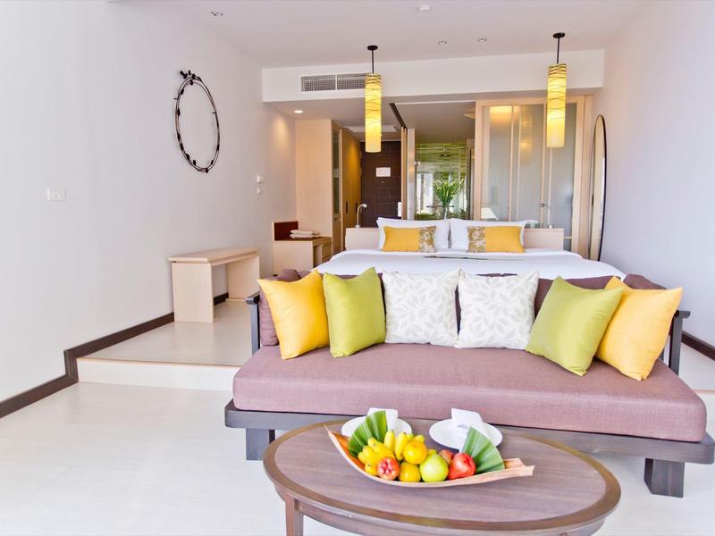 Chambre d'hôtel aménagée moderne avec canapé, coussins et assiette de fruits sur la table.