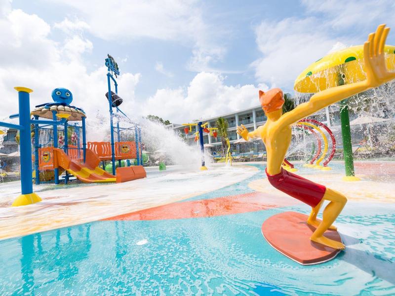 Parc aquatique avec aire de jeux d'eau, toboggans et figures colorées sous un jour ensoleillé.