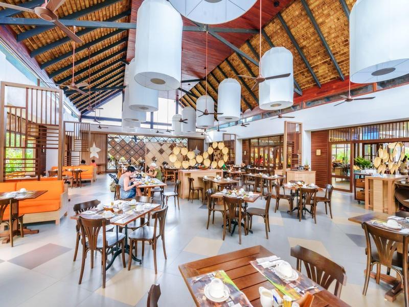 Grand restaurant lumineux avec poutres en bois, nombreuses tables et éclairage moderne.