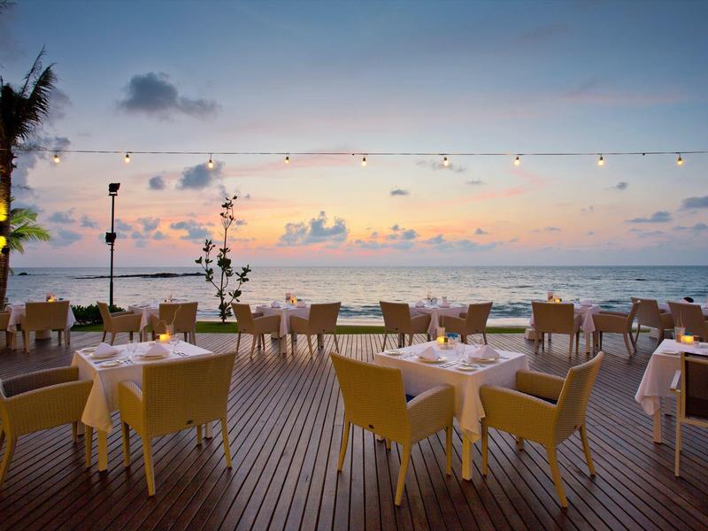 Terrasse de restaurant avec des chaises jaunes au bord de la mer au coucher du soleil.