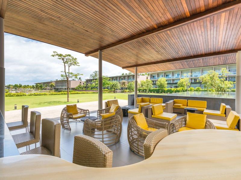 Terrasse couverte avec mobilier en rotin moderne et coussins jaunes dans une zone hôtelière avec vue sur pelouse