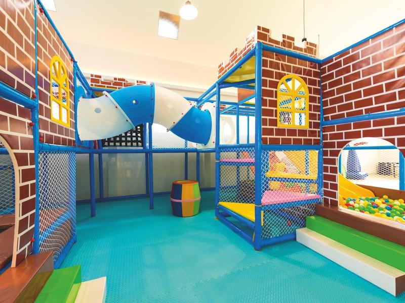 Aire de jeux intérieure colorée avec toboggans, murs d'escalade et espace assis pour enfants.