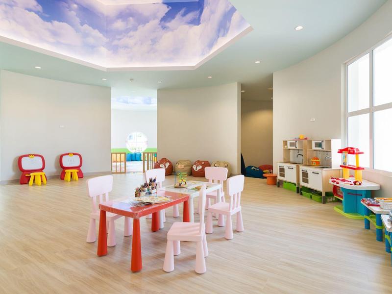 Espace de jeux pour enfants lumineux avec tables, chaises et jouets dans une pièce moderne.