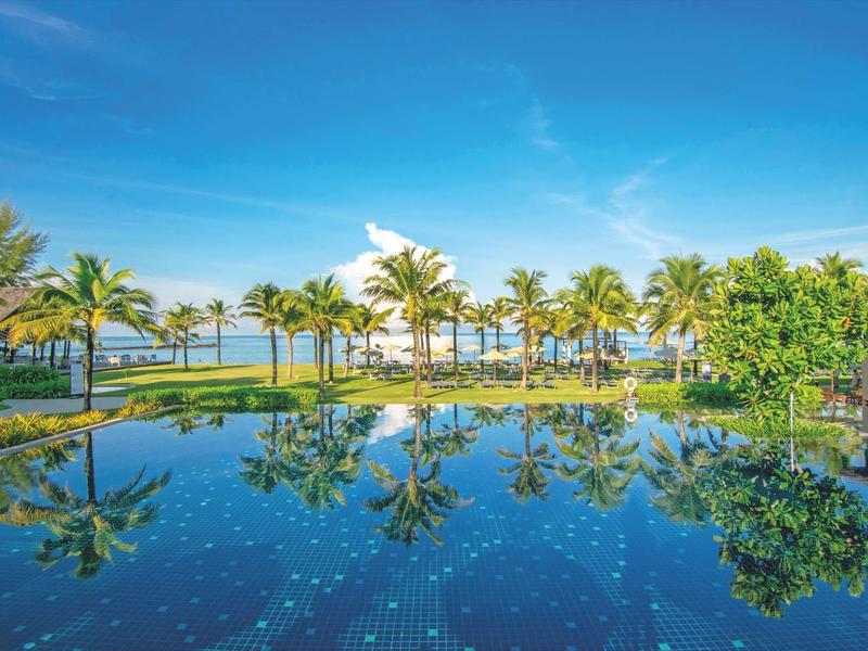 Une piscine tropicale avec des palmiers et un ciel bleu dans un complexe hôtelier.