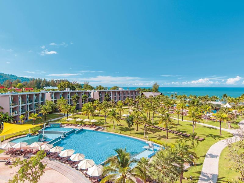Grand complexe avec piscine, palmiers et vue sur la mer sous un ciel bleu.