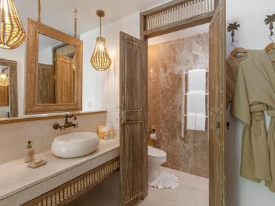 Modernes Badezimmer mit Holzdetails, weißem Waschbecken, warmen Lampen und beigen Bademänteln.