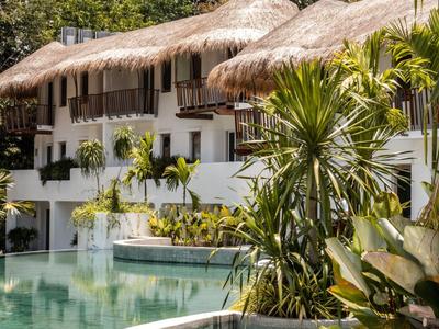 Ein tropisches Hotel mit weißen Gebäuden, Strohdächern und einem Pool, umgeben von Pflanzen.